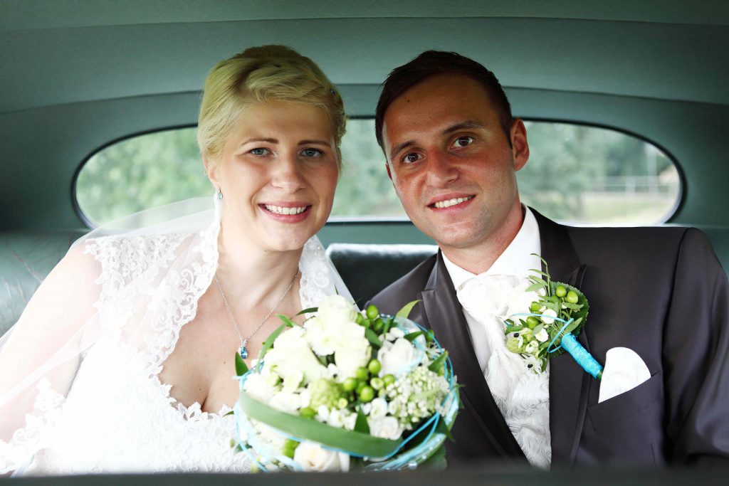 Brautpaar sitzt auf Rücksitz im Auto