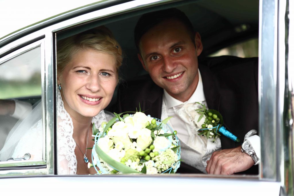 Brautpaar schaut aus SEitenfenster des Autos heraus